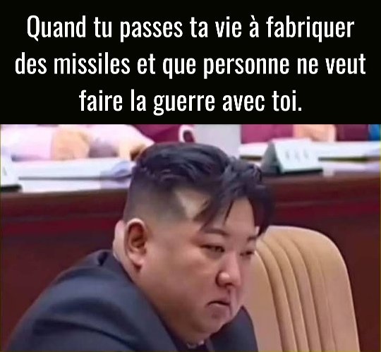 Kim Jong-un assis dans une salle de réunion, portant un costume sombre, expression triste, texte en haut : Quand tu passes ta vie à fabriquer des missiles et que personne ne veut faire la guerre avec toi.