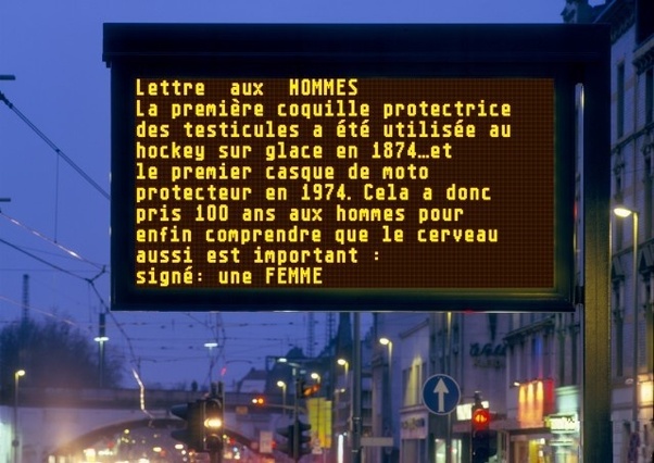 Panneau d'affichage numérique jaune dans une rue de ville la nuit affichant un texte en français.