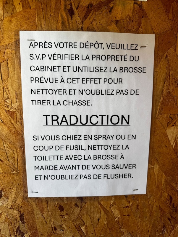 Panneau blanc sur mur en bois avec texte en français : instructions polies pour nettoyer les toilettes en haut et traduction vulgaire directe en dessous.