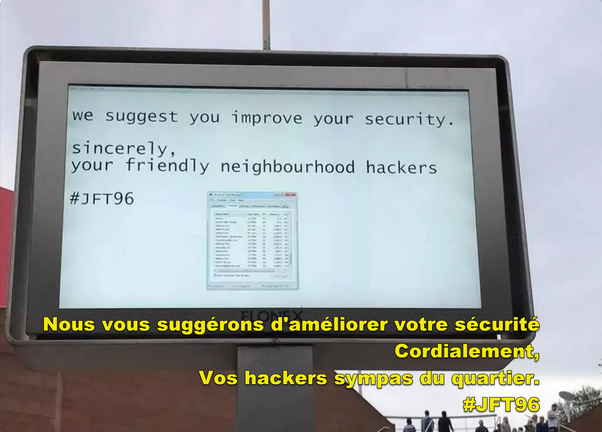 Écran publicitaire extérieur affichant un message des hackers en anglais avec traduction française en jaune en dessous.