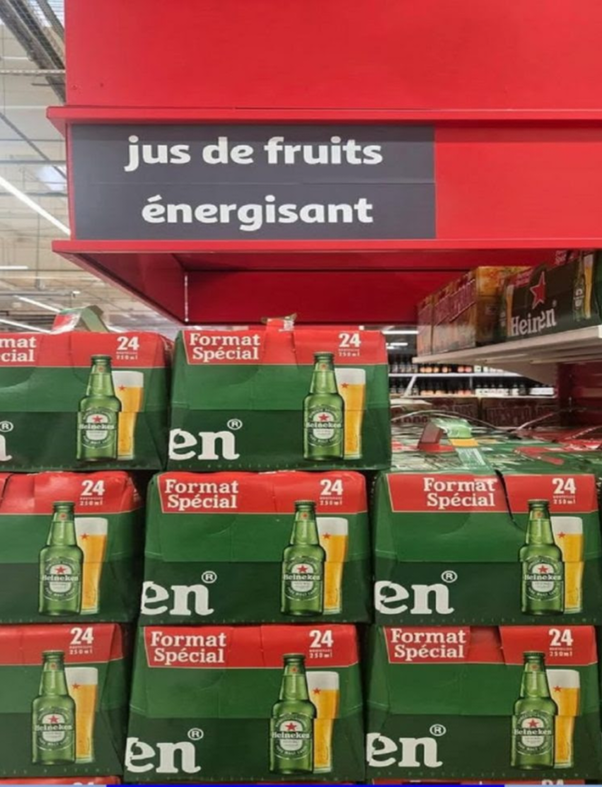 Cartons de Heineken empilés sous une enseigne 'jus de fruits énergisant' dans un rayon de supermarché.