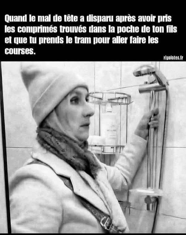 Photo en noir et blanc d'une femme en bonnet, écharpe et manteau tenant une pomme de douche dans une salle de bain carrelée.